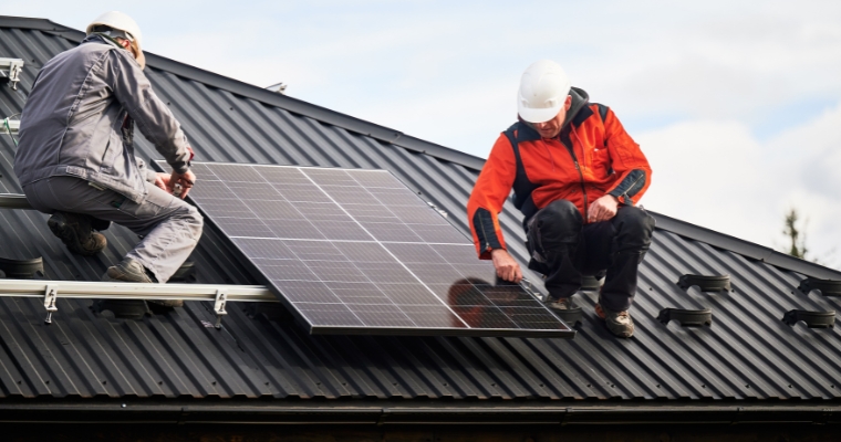 Two men on a rooftop working with solar panels, showcasing the positive community impact of sustainable housing in Montana.