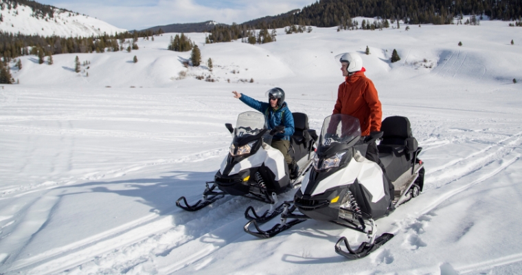 Two people riding snowmobiles through a snowy landscape in Whitefish, Montana, showcasing winter adventure tours.