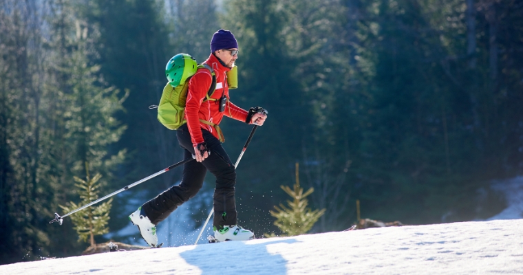 A person carrying skis and a backpack walks on a snowy hill, showcasing the snowshoeing experience in Whitefish, Montana.