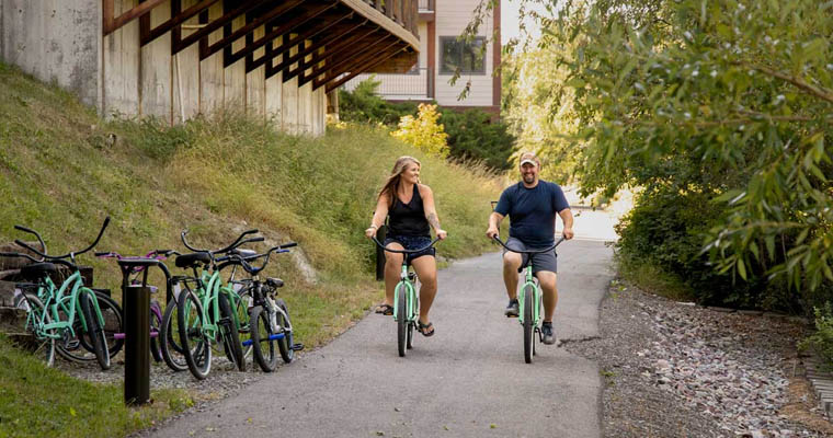 Tourist couples enjoy cycling near the river in The Pine Lodge on Whitefish