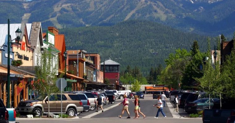 People stroll along the street in Downtown Whitefish, with a majestic mountain backdrop during a historical walking tour.