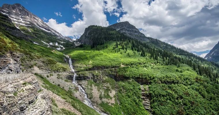 A picturesque waterfall cascades down a mountainside, showcasing the natural beauty along Going-to-the-Sun Road in Whitefish, Montana.