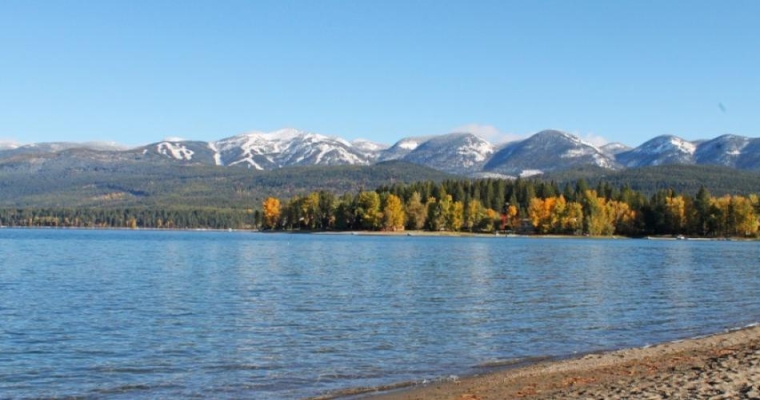 A serene lake surrounded by mountains and trees, showcasing the natural beauty of Whitefish City Beach in Montana.