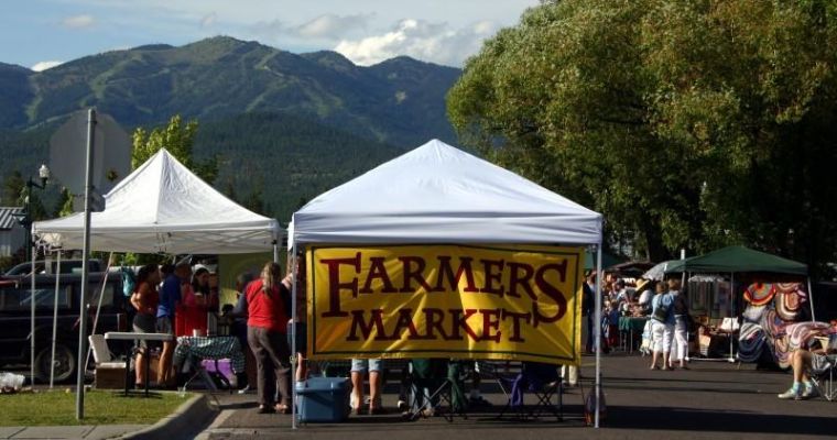 Scenic view of a bustling farmers market in the mountains of Whitefish, Montana, featuring fresh local goods and community spirit.