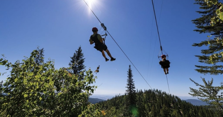 The tourists experience the thrill of ziplining through the picturesque mountains at Whitefish Mountain Resort.