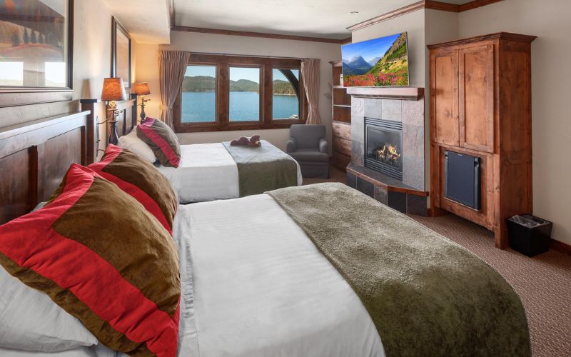 Two beds in a cozy room featuring a fireplace and a television, perfect for relaxing during the Whitefish Arts Festival.