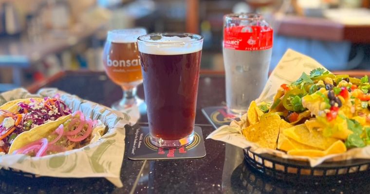 A table displaying two baskets of food alongside a beer, highlighting local brews at Bonsai Brewing Project in Whitefish, Montana.