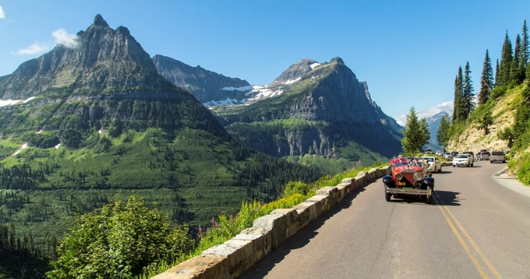 A vehicle travels along a picturesque mountain road, surrounded by stunning peaks, highlighting the scenic drive in Whitefish, Montana.