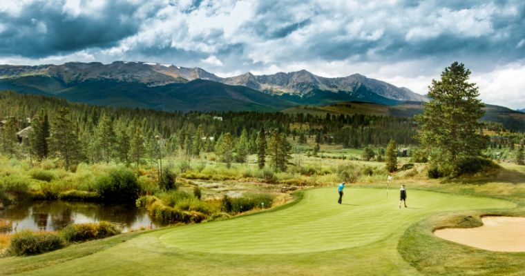 A picturesque golf course at Whitefish Lake Golf Club, framed by stunning mountains in the distance.