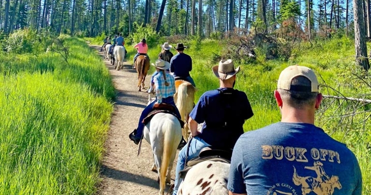 A group of tourist enjoy horseback riding along a scenic trail in the woods, highlighting outdoor activities at Bar W Guest Ranch, Whitefish, Montana.