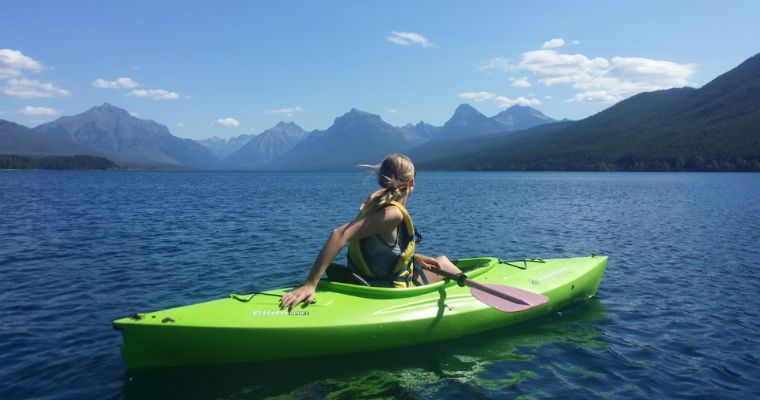 A woman kayaks on a serene lake, surrounded by majestic mountains, showcasing the beauty of Whitefish, Montana.