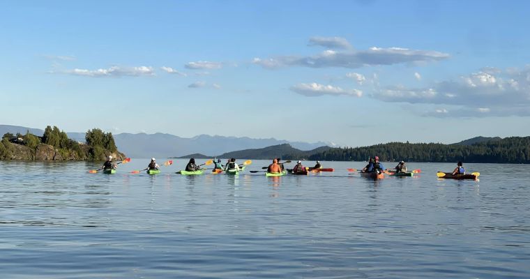 A group of individuals paddling in kayaks on a serene lake, showcasing the beauty of outdoor activities in Whitefish, Montana.