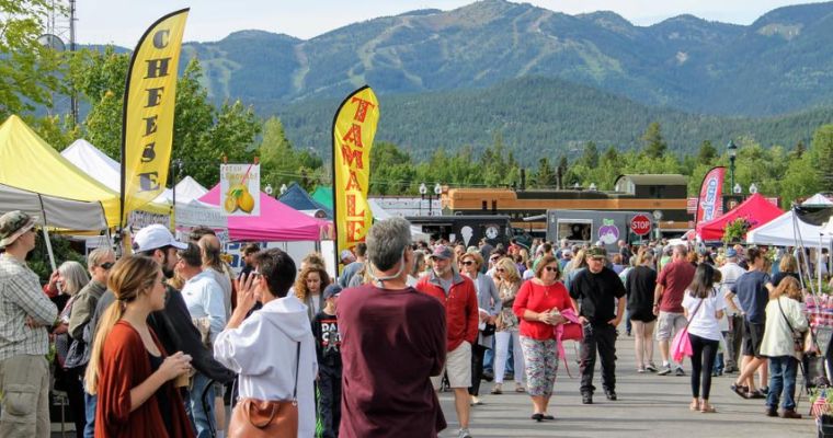 Visitors stroll through the lively Whitefish Farmers Market, exploring various stalls and enjoying the outdoor shopping experience.