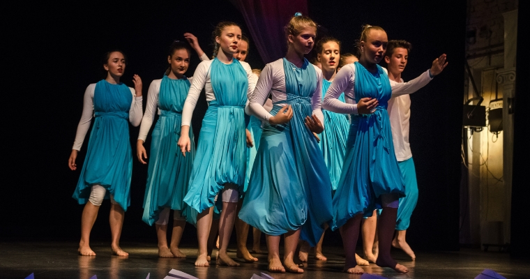 A group of young performers in blue dresses standing on stage at the Whitefish Theatre Company in Montana.