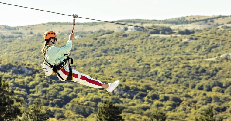 A person glides on a zipline, soaring over a scenic mountain landscape in Whitefish, Montana.