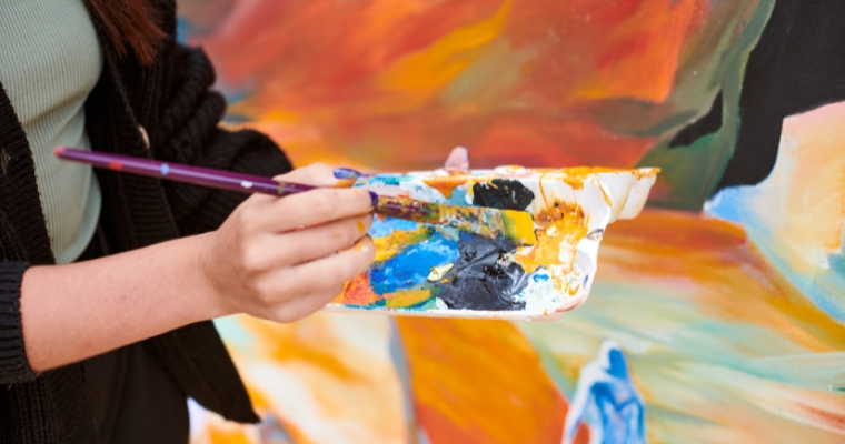 A woman painting on a large canvas with a paintbrush at the Whitefish Arts Festival, showcasing her artistic talent.