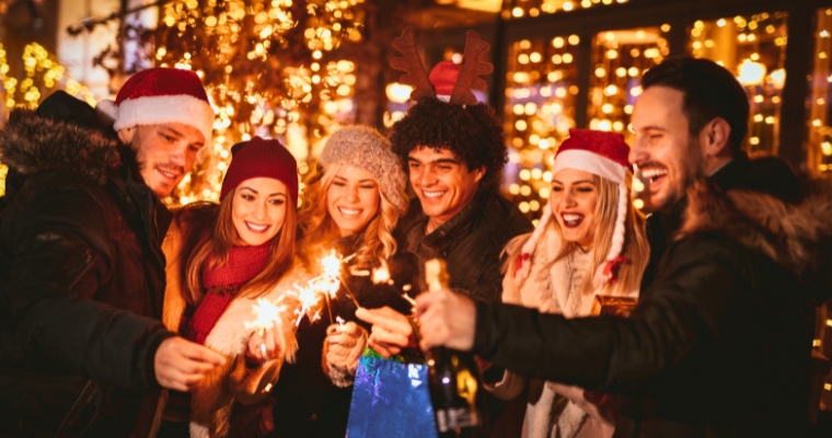 A cheerful gathering of people with sparklers illuminated by vibrant Christmas lights in Whitefish, Montana.