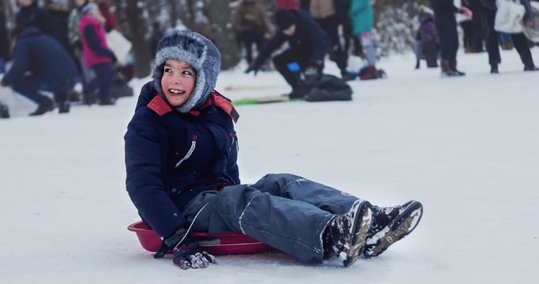 A young boy enjoys sliding down a snowy hill on a sled, showcasing the family-friendly winter activities in Whitefish, Montana.