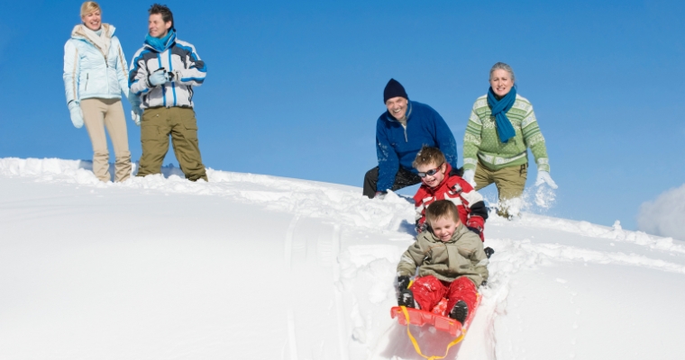 A family joyfully sleds down a snowy slope during a festive Christmas in Whitefish, Montana.