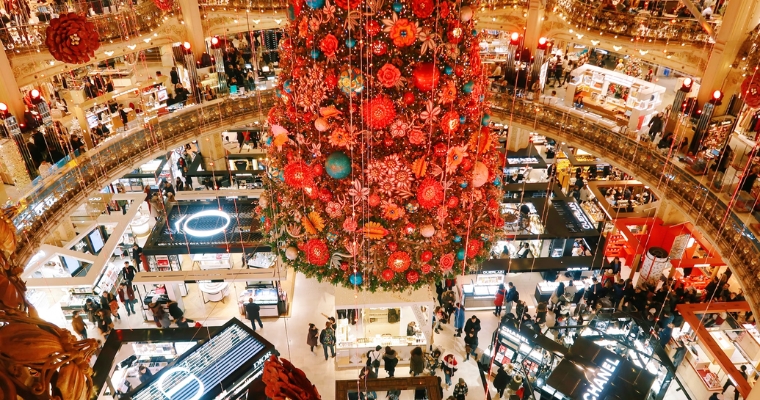 A vibrant Christmas tree in a crowded mall, surrounded by shoppers looking for distinctive holiday gifts in Whitefish, Montana.