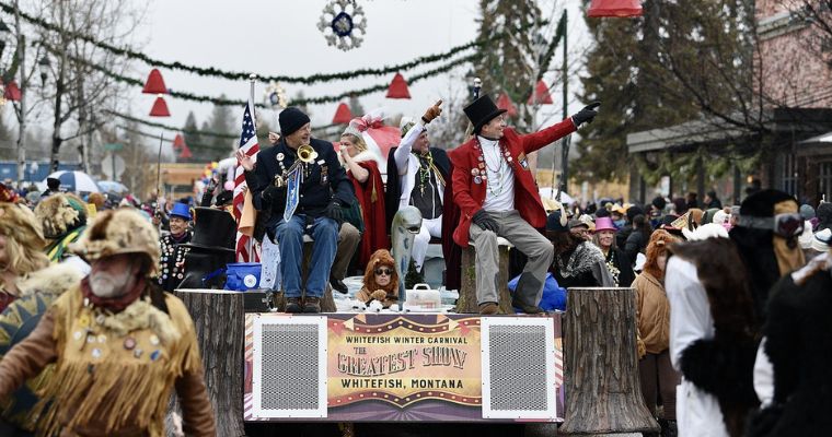 A festive float carries people in costumes, showcasing the spirit of the Grand Parade at the Whitefish Winter Carnival.