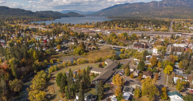 Aerial view of a picturesque town nestled among lush trees and majestic mountains, highlighting its investment property Whitefish potential.