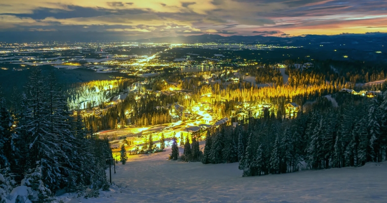 Nighttime city lights illuminate the landscape, viewed from a ski slope in Whitefish, highlighting the area's investment potential.