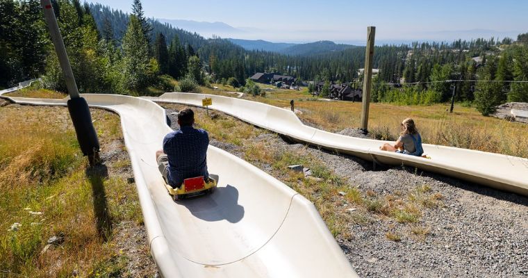 Two people enjoying a thrilling ride down an alpine slide on a sunny summer day in Whitefish.