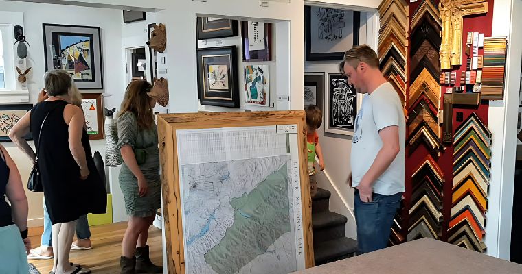 Visitors exploring framed art pieces in a Whitefish gallery during the summer exhibition season.