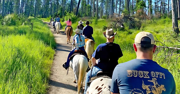 A diverse group of tourist rides horses along a beautiful summer trail in Whitefish, showcasing outdoor adventure.