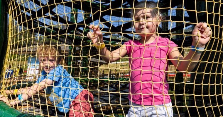 Two children joyfully play in a net at the Spider Monkey Mountain playground in Whitefish in summer.