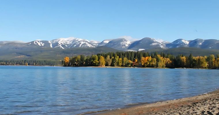 Scenic view of Whitefish Lake, framed by mountains and trees, ideal for summer relaxation and sunbathing.