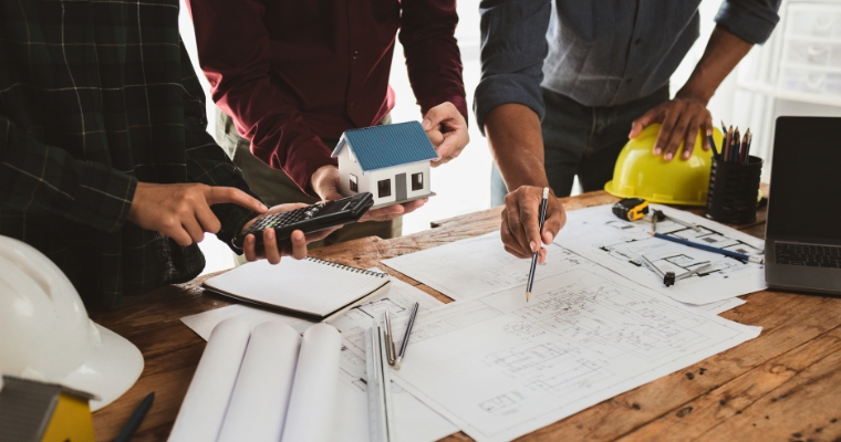 Three professionals collaborate on a luxury home project, examining a detailed house model in a design meeting.