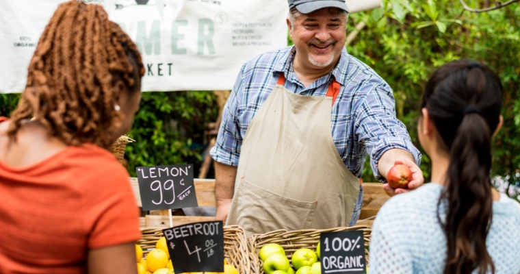 A man is selling fresh goods to a woman at a vibrant summer farmer's market in Whitefish.