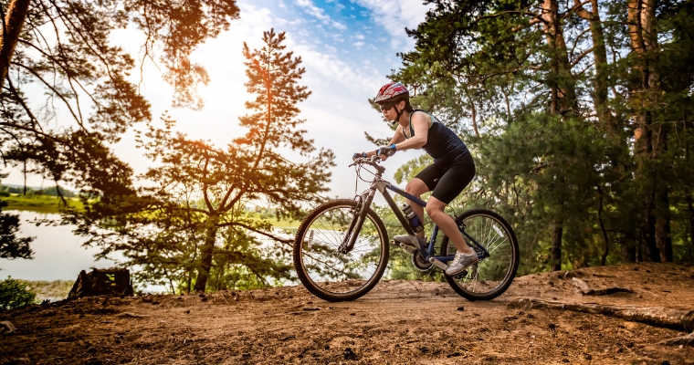 A man mountain biking on a dirt trail in Whitefish, surrounded by vibrant summer scenery and natural beauty.