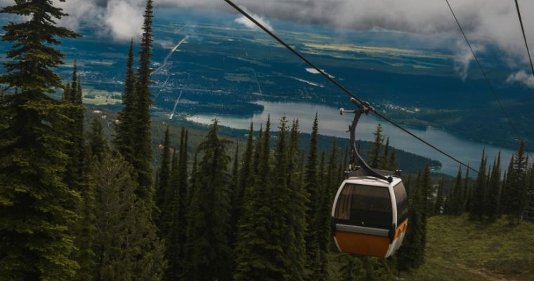 A scenic gondola ride in Whitefish MT, gliding over lush trees and sparkling water against a stunning mountain backdrop.