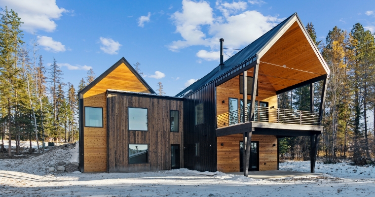 A stylish cabin in a wintery forest setting, with snow blanketing the ground at 158 Mountain Brook Lane, Whitefish.