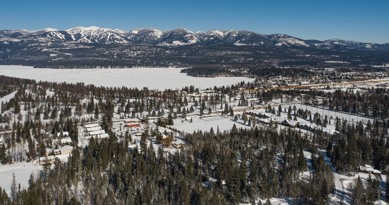 Aerial perspective of a snowy mountain range alongside a town, emphasizing the sustainable living concept at Little Bear, Whitefish.