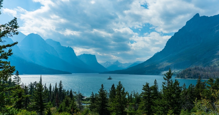 A picturesque lake bordered by mountains and greenery, representing the natural beauty of Glacier National Park.