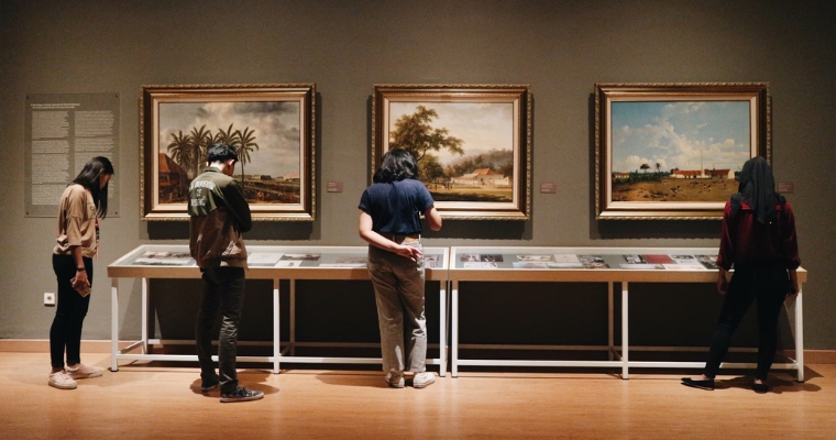 Visitors admire various paintings in an art museum, showcasing cultural and artistic opportunities in Whitefish, Montana.