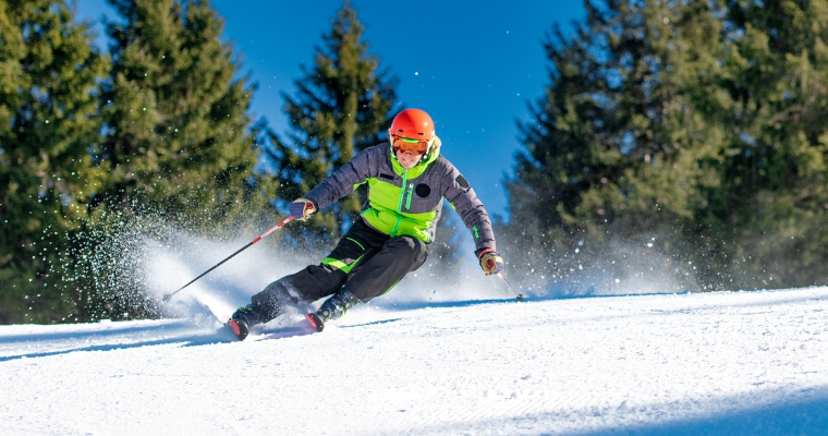 A skier in a bright green jacket and orange helmet navigates a snowy slope, highlighting outdoor adventures in Whitefish, Montana.