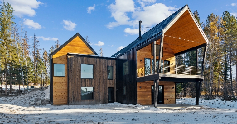 A contemporary cabin surrounded by snow-covered trees, highlighting investment potential in Whitefish, Montana.