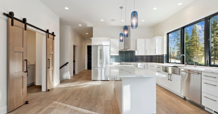 A modern kitchen featuring white cabinets and warm wood floors, part of a home-building project in Montana.