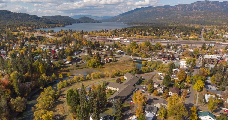 Aerial perspective of a town encircled by trees and mountains, showcasing the picturesque setting of Whitefish, MT.