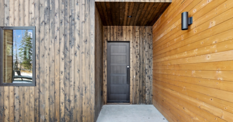 Exterior view of a wooden wall with a black door, part of a Net-Zero Home in Whitefish, Montana, showcasing sustainability.