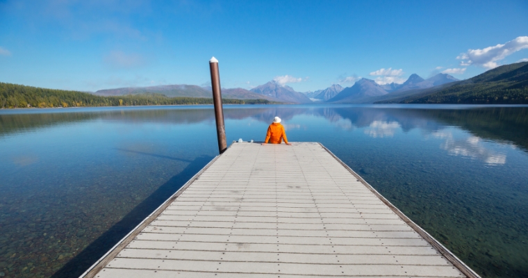 A person on a dock, looking out at a peaceful lake in downtown Whitefish, Montana, enjoying the scenic surroundings.